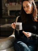 Two hands holding a traditional grey and white stoneware mug thrown by John Ryan